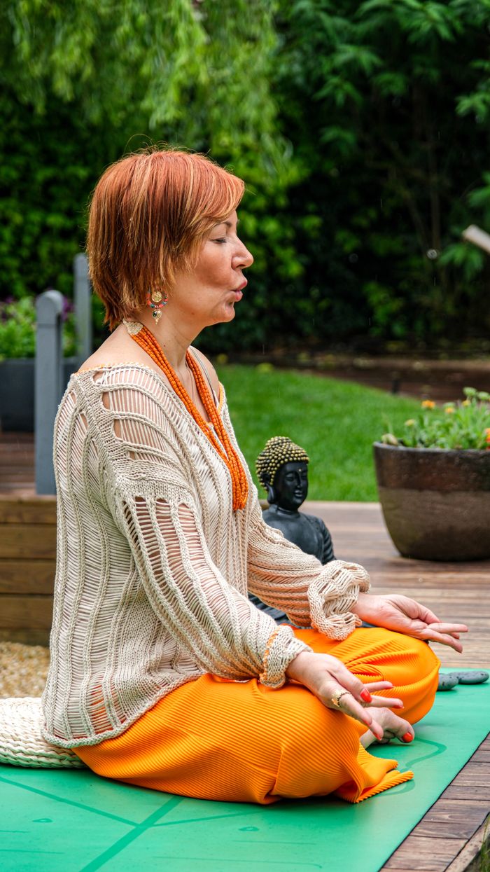 Woman meditating outdoors on a yoga mat with a peaceful garden backdrop.