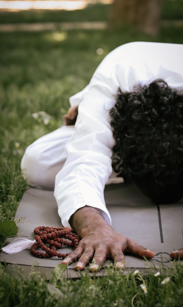A person practicing yoga and meditation outdoors with prayer beads on a grass mat.