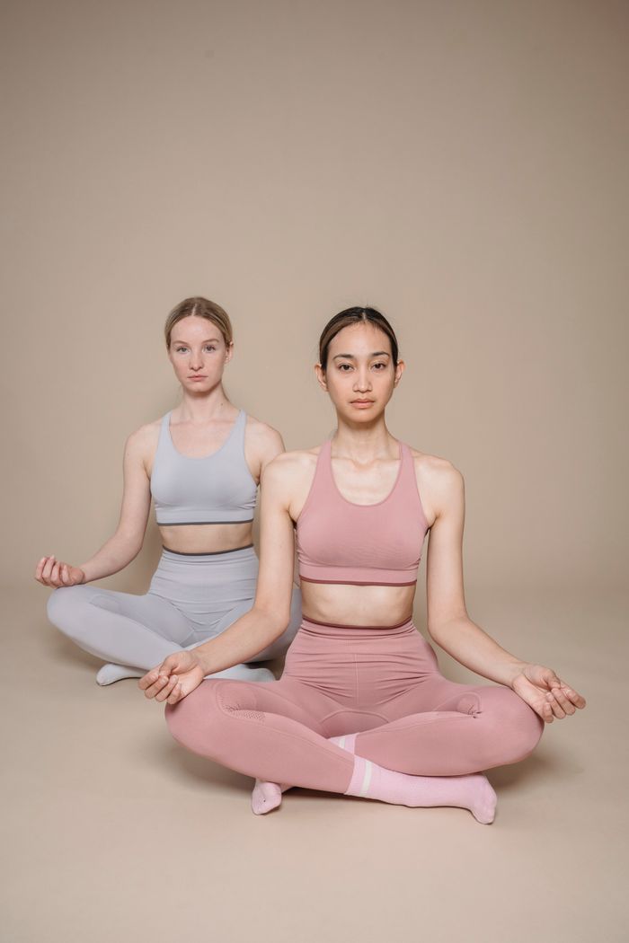 Two women in activewear meditating indoors, focusing on mindfulness and wellness.